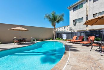 A small pool with a brown umbrella and chairs around it.